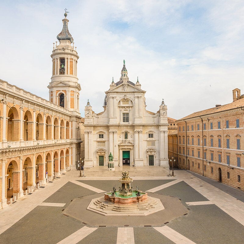 Square of Loreto, Basilica della Santa Casa in sunny day, portico to the side, people in the square in Loreto, Ancona, Italy